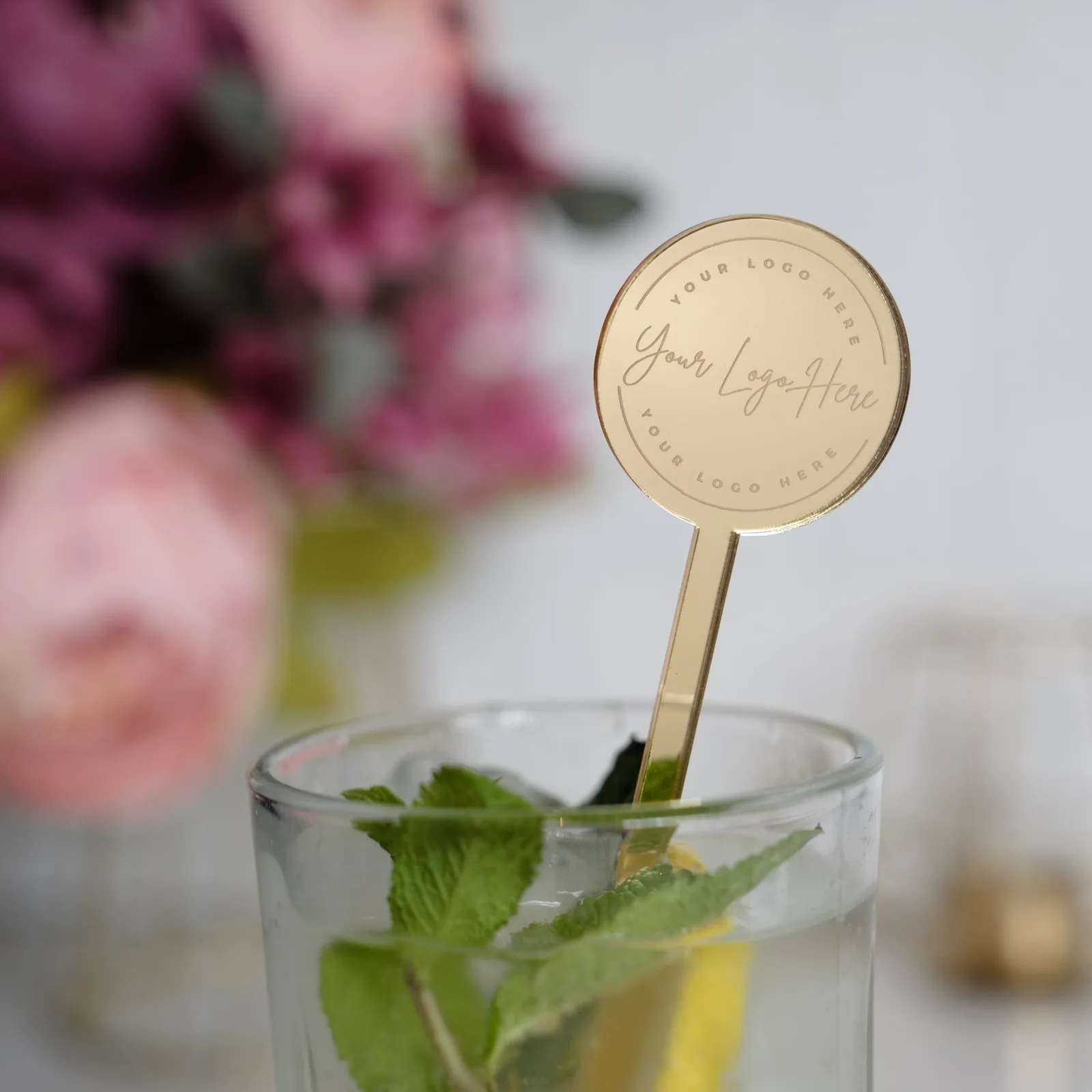 Mirror gold round-headed stirrer engraved with a logo, standing in a glass with mint
